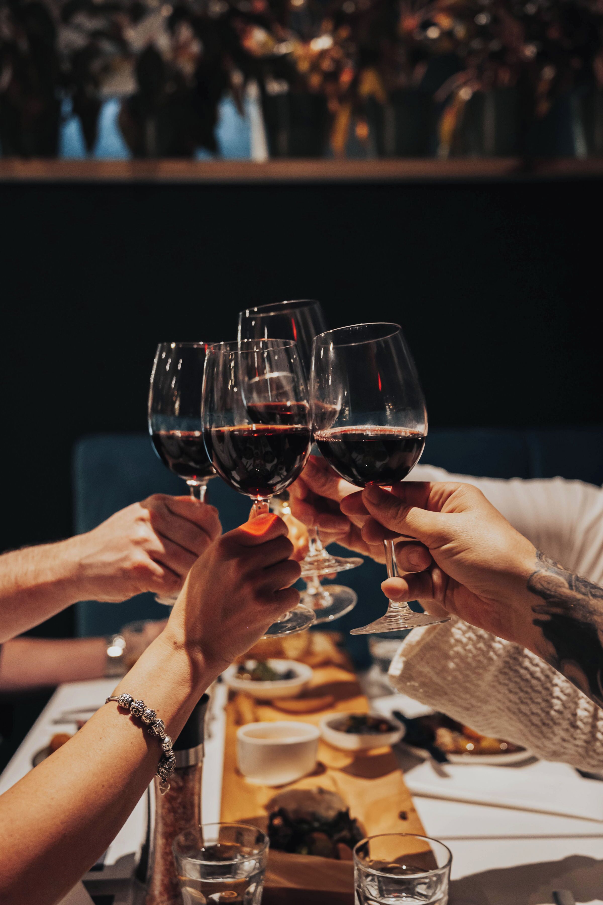 A group of people toasting with wine glasses at a table with a bottle of wine and a glass of water.