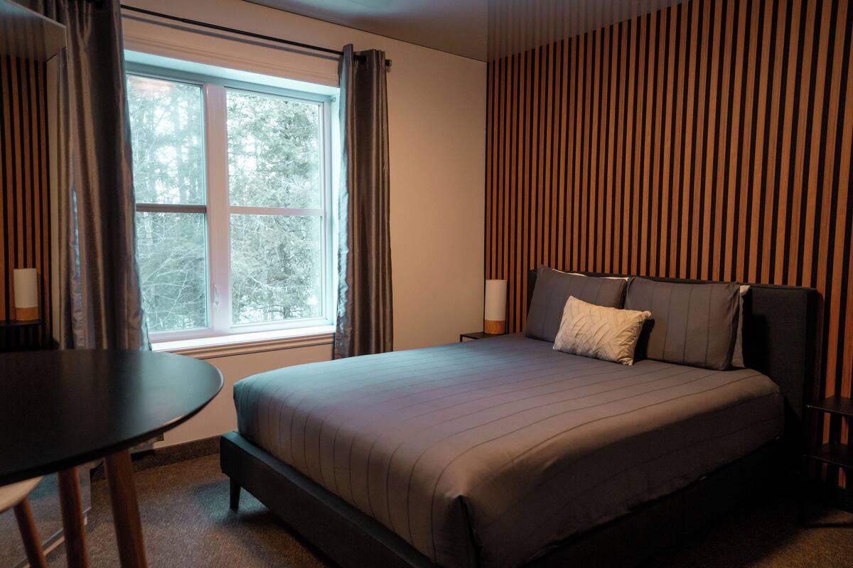 A modern hotel room with a large bed, a small table, and a window with curtains.
