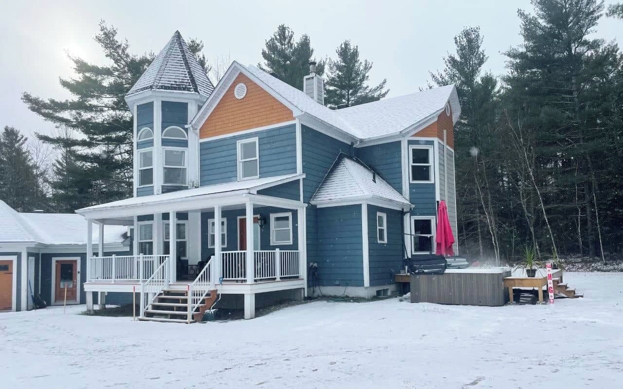 A two-story house with a porch, a hot tub, and a chimney.