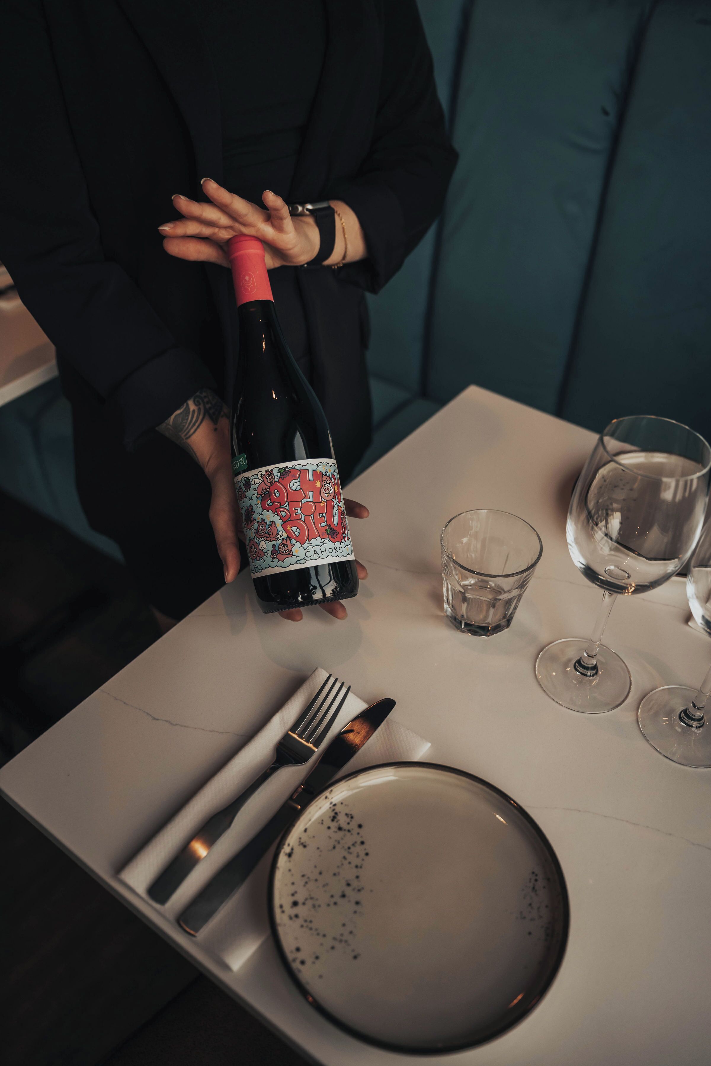 A table set for two with a bottle of wine, two glasses, a fork, a knife, and a plate.