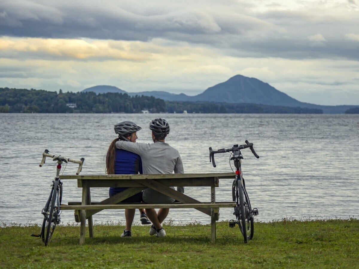 Two people sitting on a bench by a lake with bicycles.
