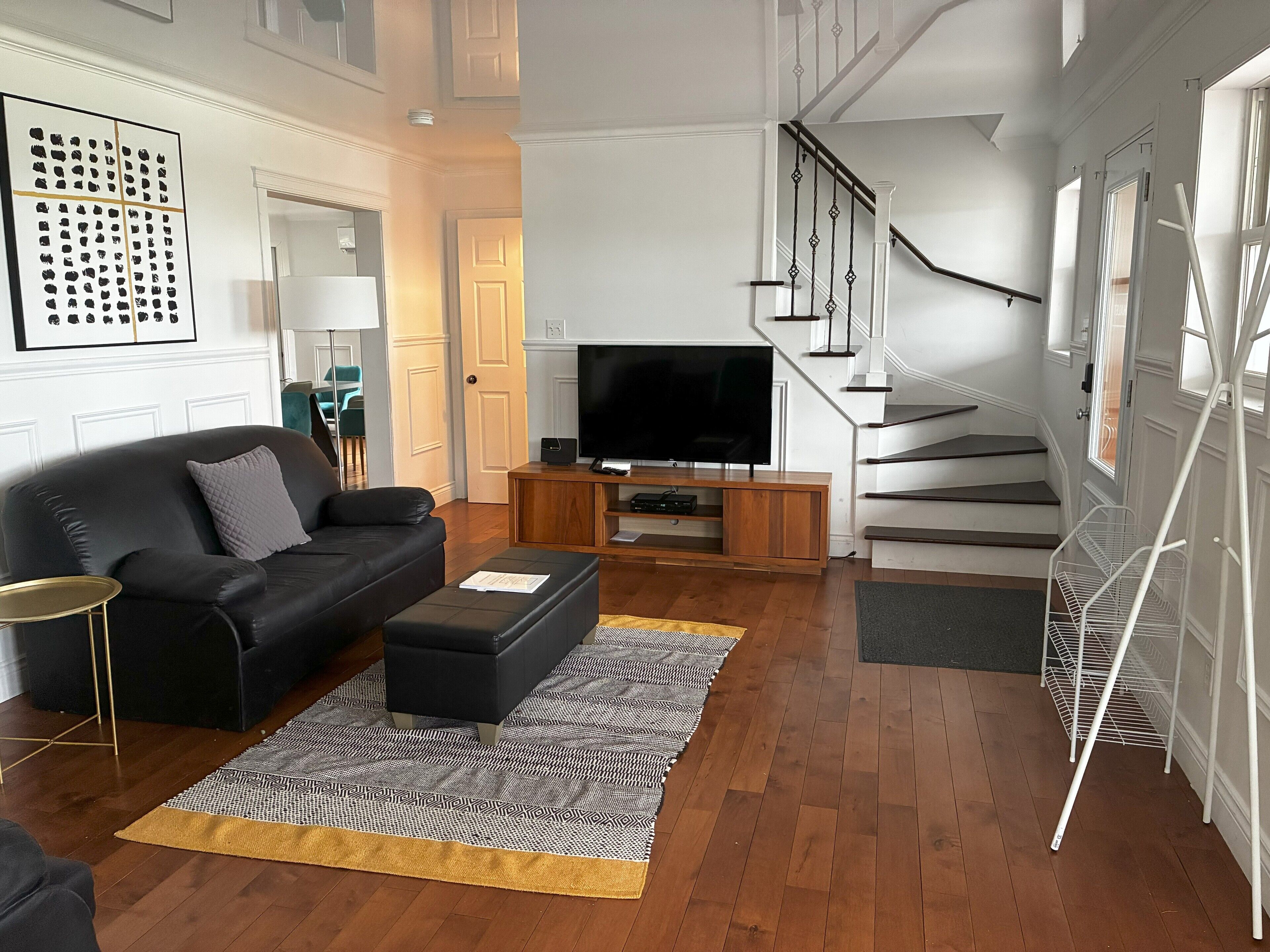 A modern living room with a black leather sofa, a wooden entertainment unit, and a staircase with white railings.