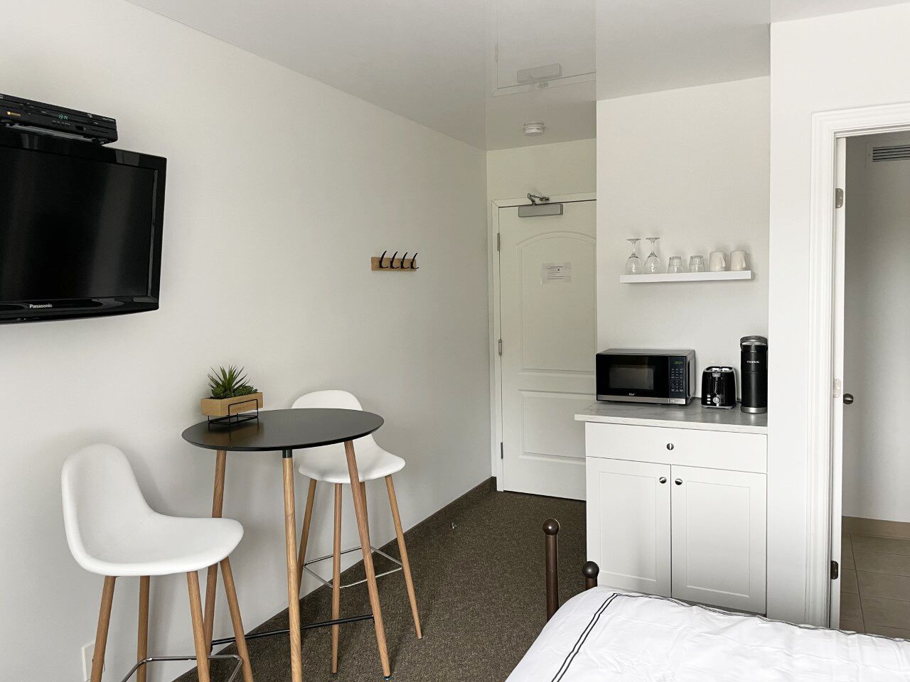 Camera d'albergo compatta con un letto, un piccolo tavolo da pranzo con due sedie, una TV a parete, un forno a microonde e una macchina del caffè sul bancone.