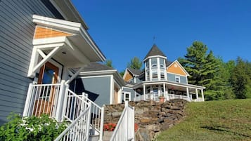 Ein zweistöckiges Haus mit einer Steintreppe zum Eingang, einem markanten Turm und einem gepflegten Rasen.