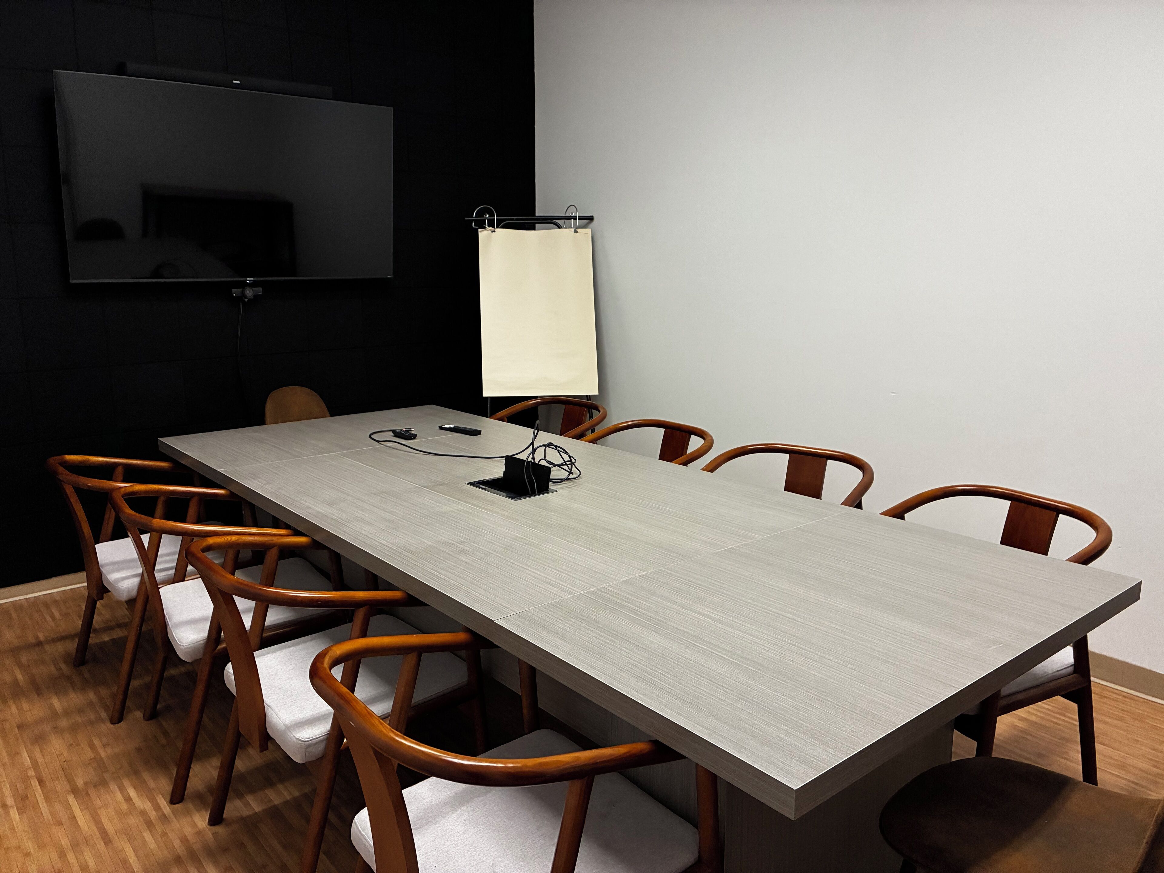 A conference room with a long table, six wooden chairs, a flat-screen TV on the wall, and a whiteboard.