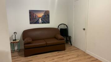 Una habitación con un sofá de cuero marrón, una mesita con una lámpara, una silla y una puerta.