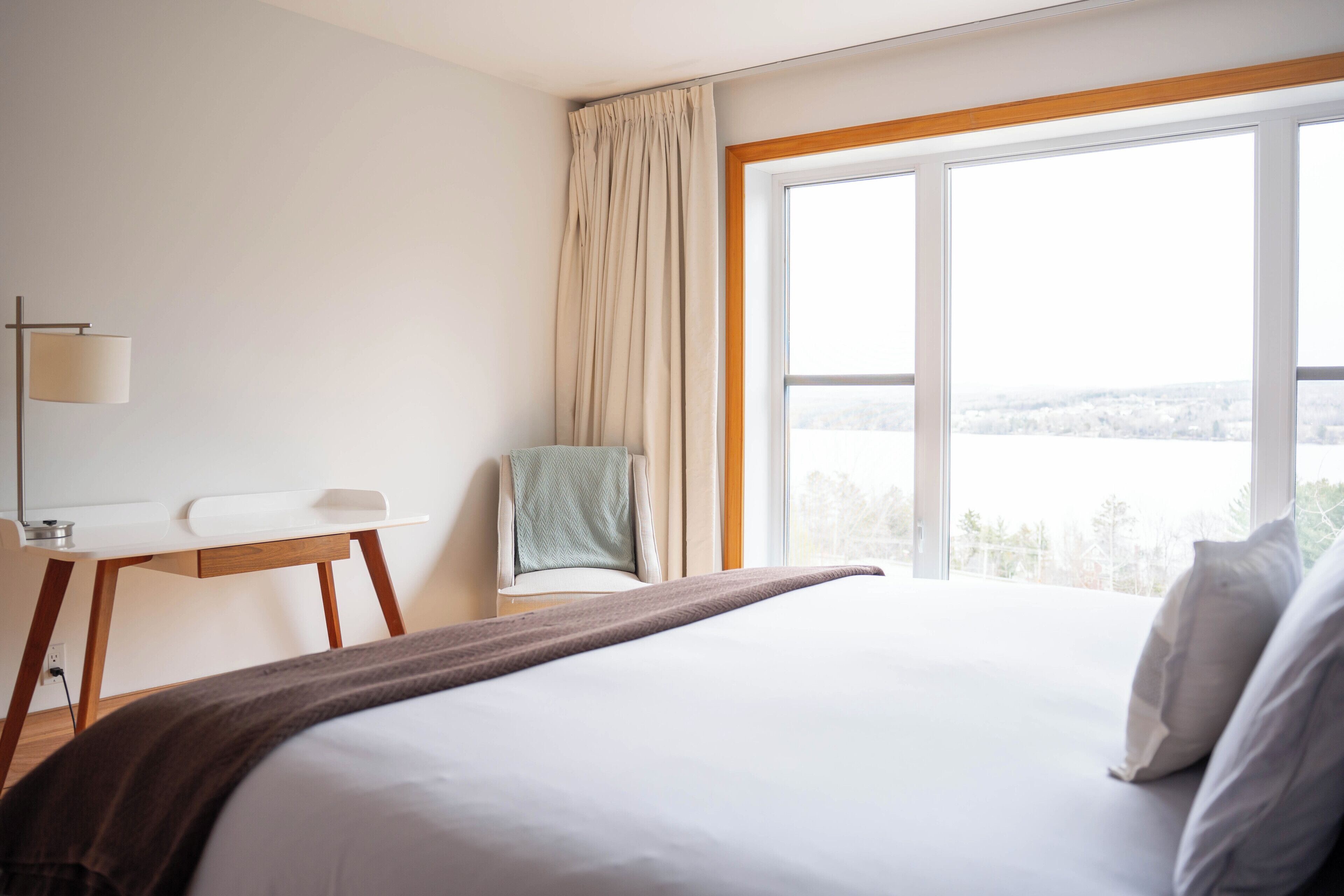 A hotel room with a large bed, a desk, a chair, and a window with a view of a snowy landscape.