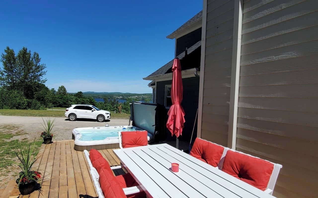 A patio with a hot tub, a table, and red cushions. A white car is parked in the background.
