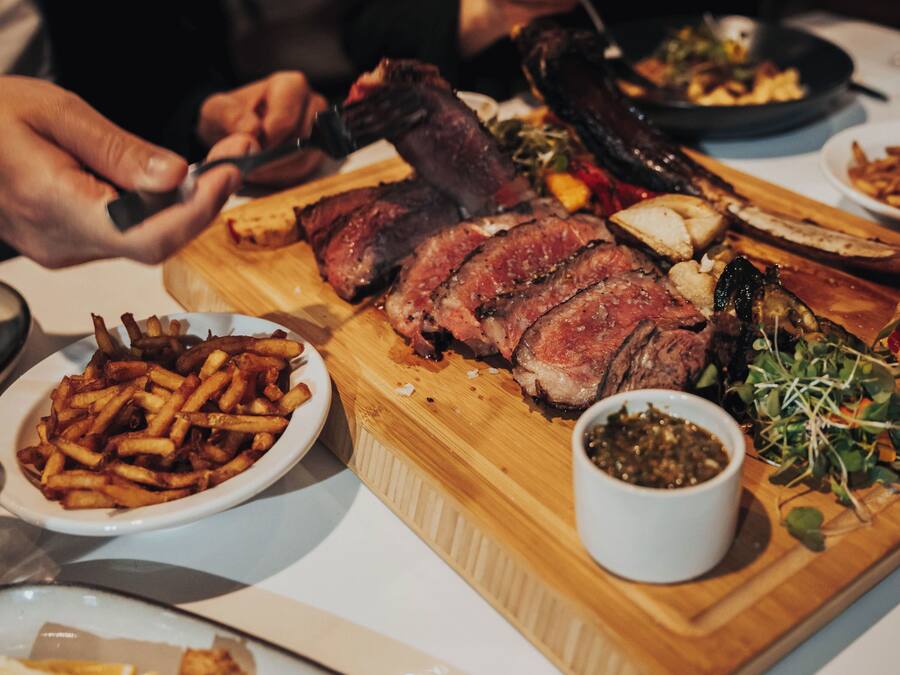 Una mesa de comedor con un gran trozo de carne, un bol de papas fritas y un recipiente pequeño con salsa.