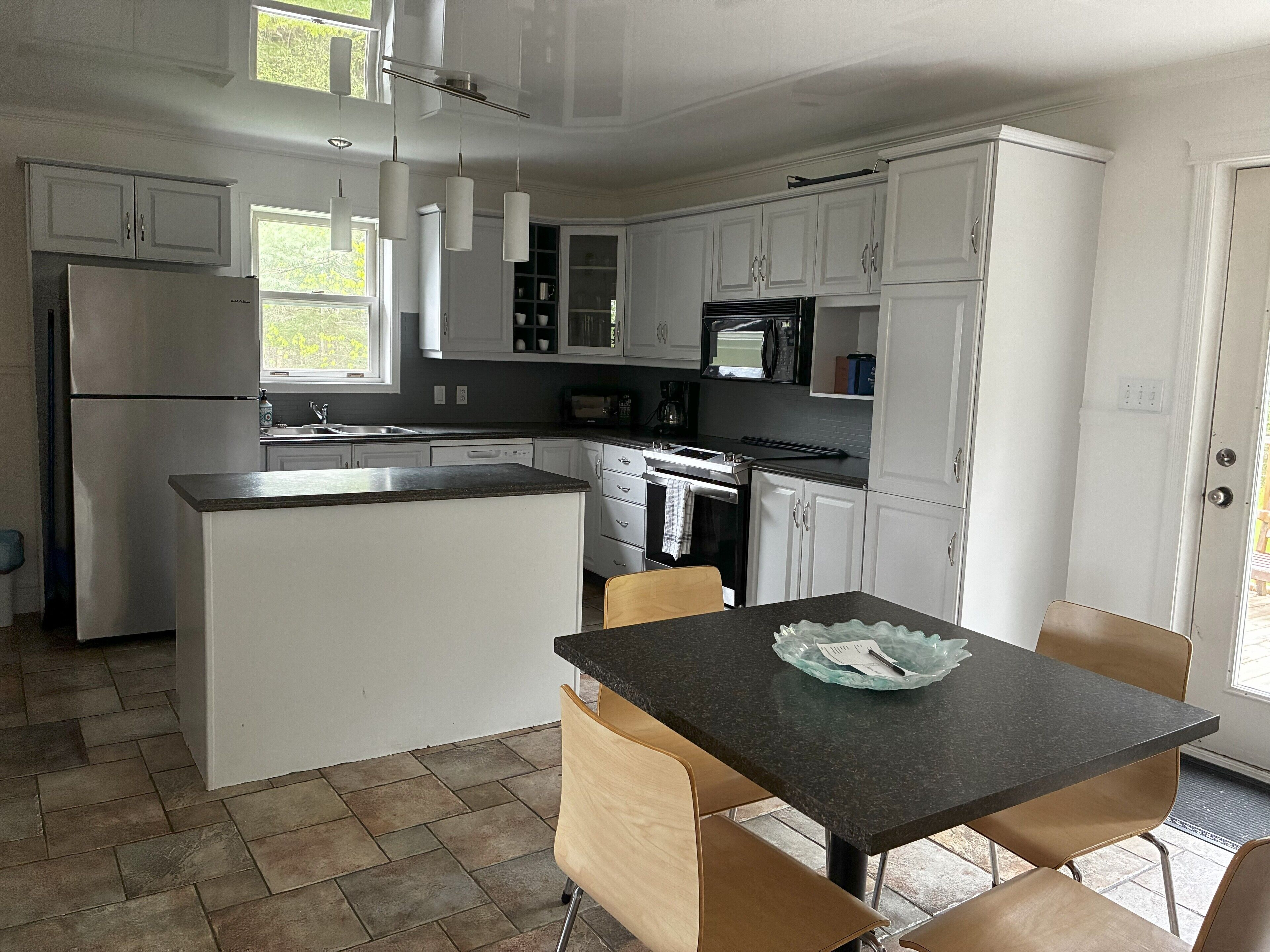 A modern kitchen with white cabinetry, a central island, a dining area with two chairs, and a built-in microwave.