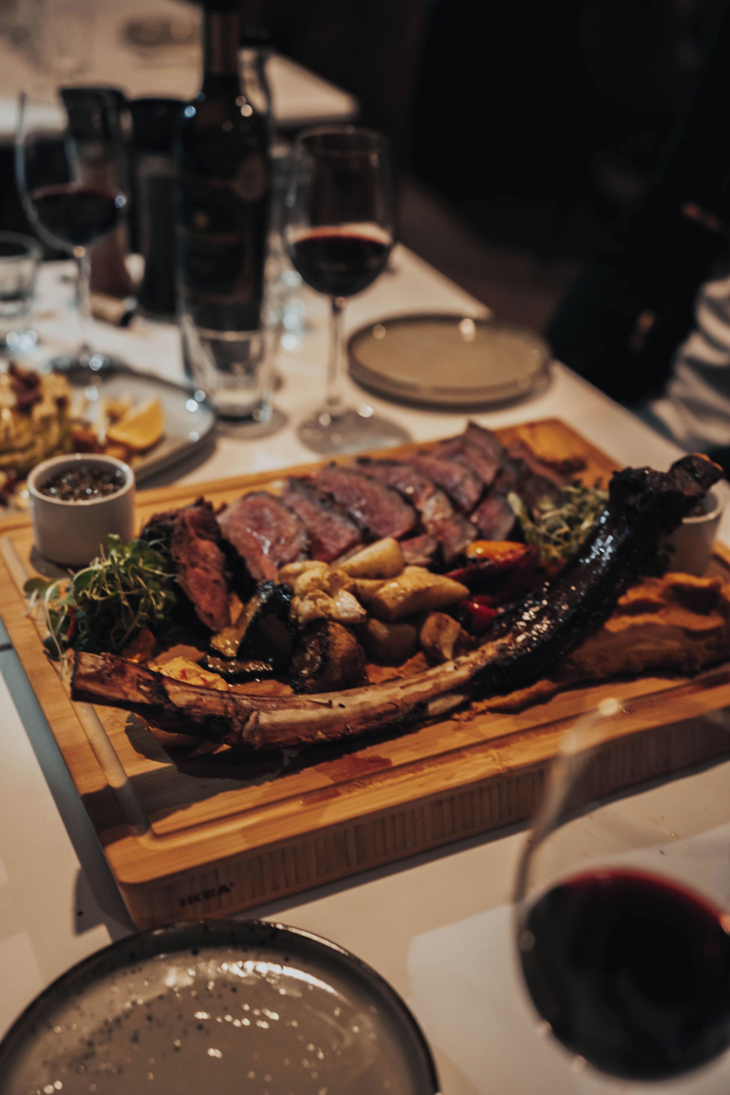 Una mesa de comedor con un gran plato de comida, incluyendo carne y verduras, además de varias copas y botellas de vino.
