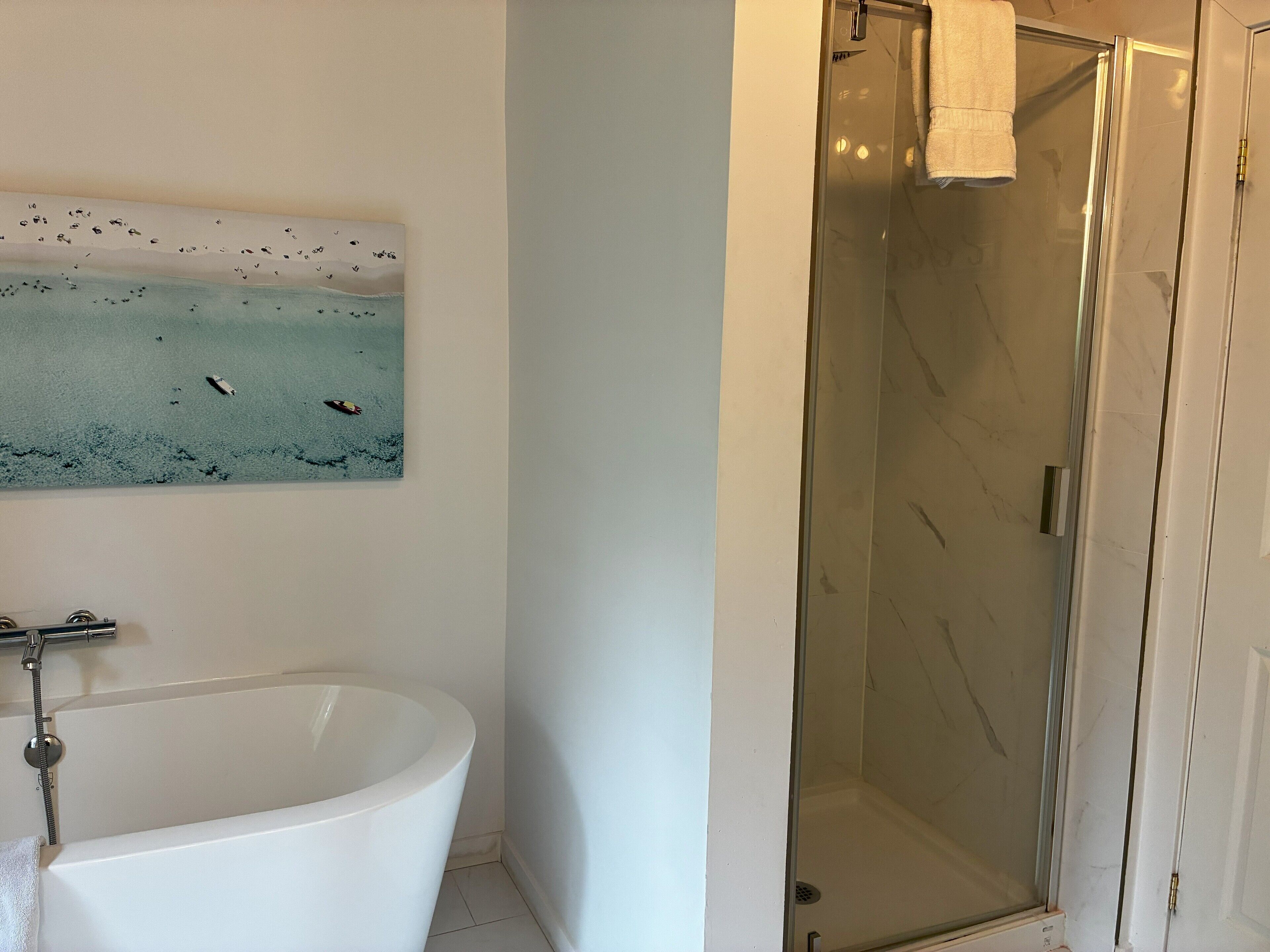 Un baño con bañera, cabina de ducha de vidrio y una obra de arte colgada en la pared.