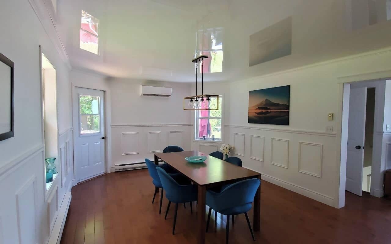 A dining area with a wooden table and blue chairs, white walls, and a painting on the wall.