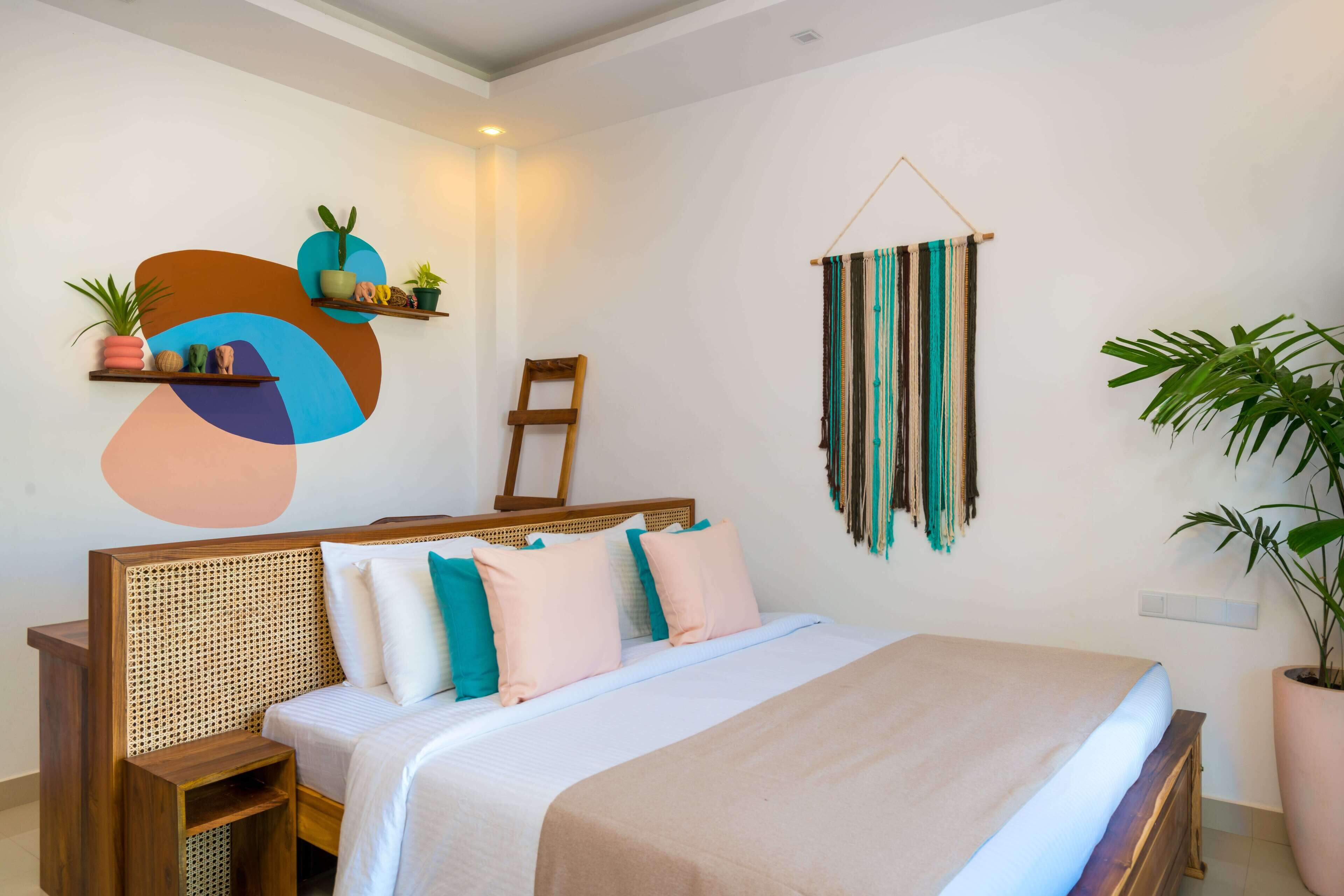A bedroom with a bed, bedside tables, a wall-mounted shelf with plants, a hanging tapestry, and a potted plant.