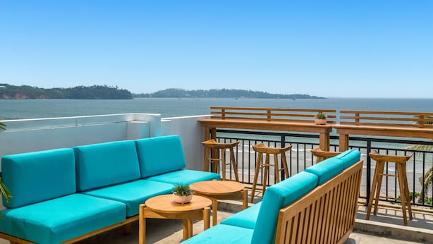 A balcony with turquoise seating, wooden tables, and a view of the sea. - Outpost Weligama Beachfront (Weligama)