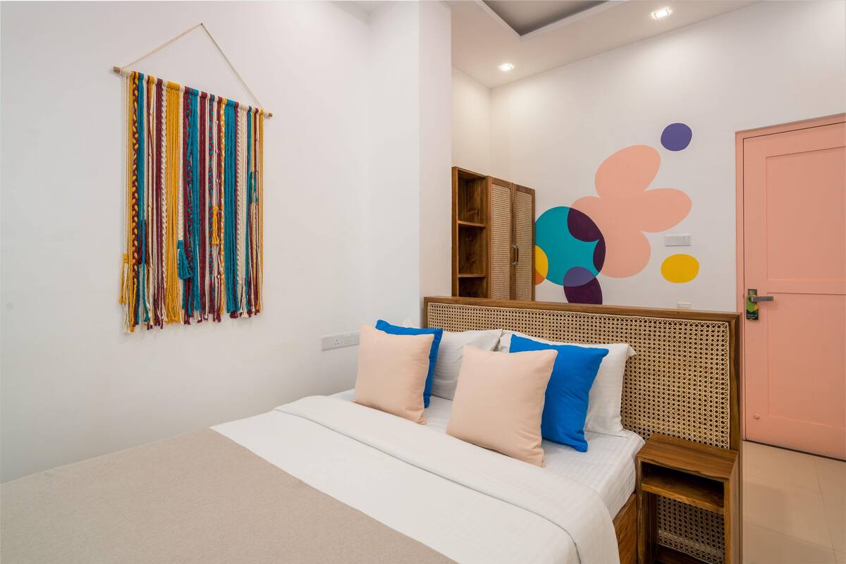 A bedroom with a bed, pillows, a wall hanging, a wardrobe, and a door.