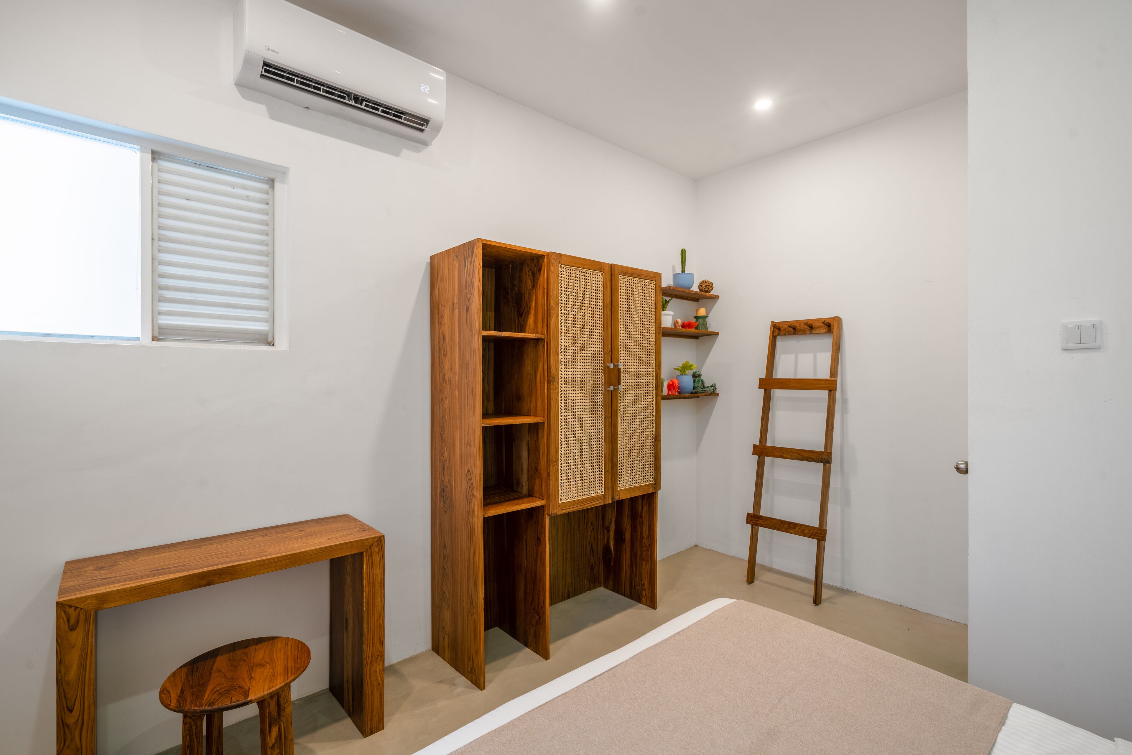 Une pièce avec une armoire en bois, une petite table, une échelle et une fenêtre avec des stores.
