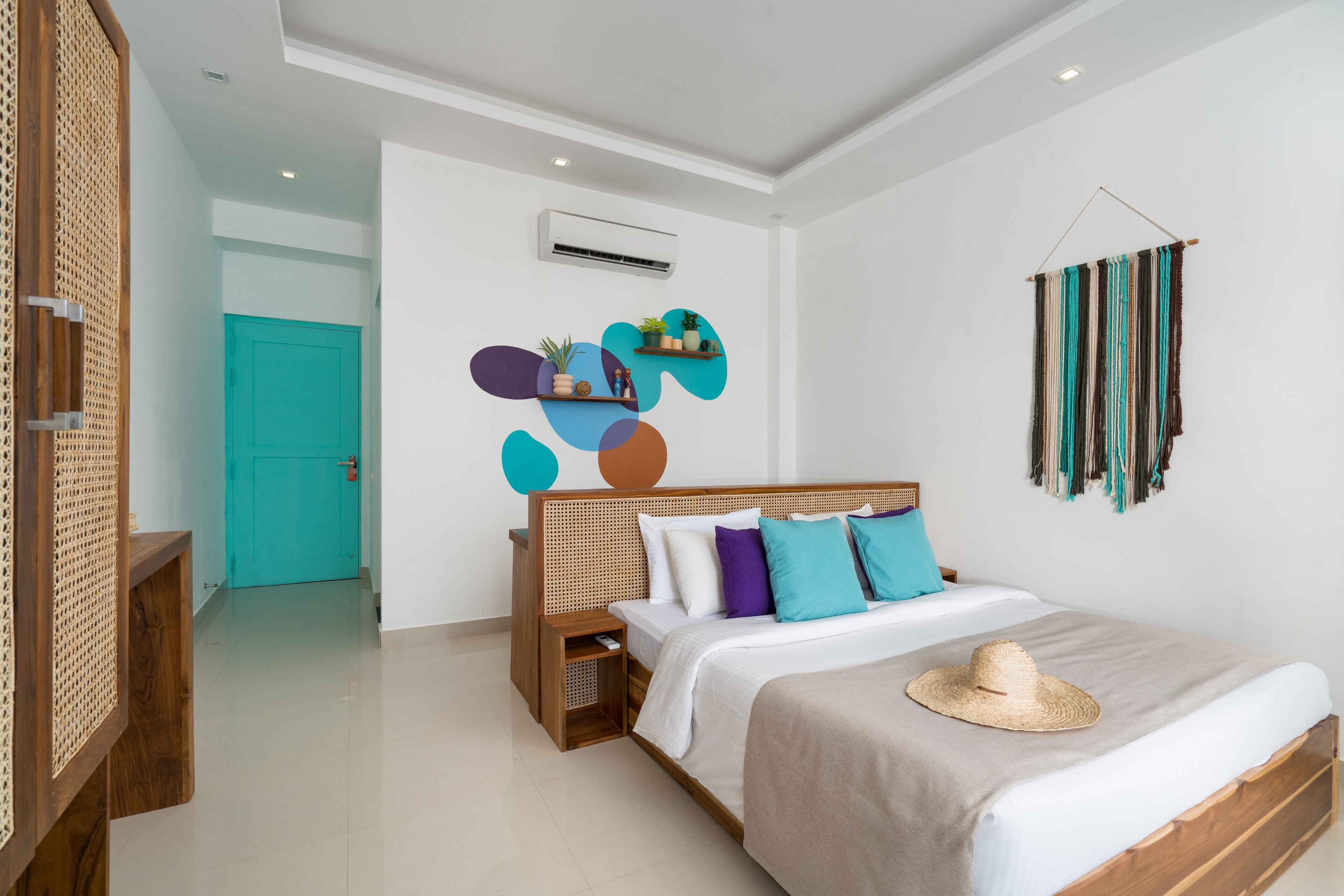 Un dormitorio moderno con cama de madera, ropa de cama blanca, una puerta color turquesa y arte abstracto en la pared.