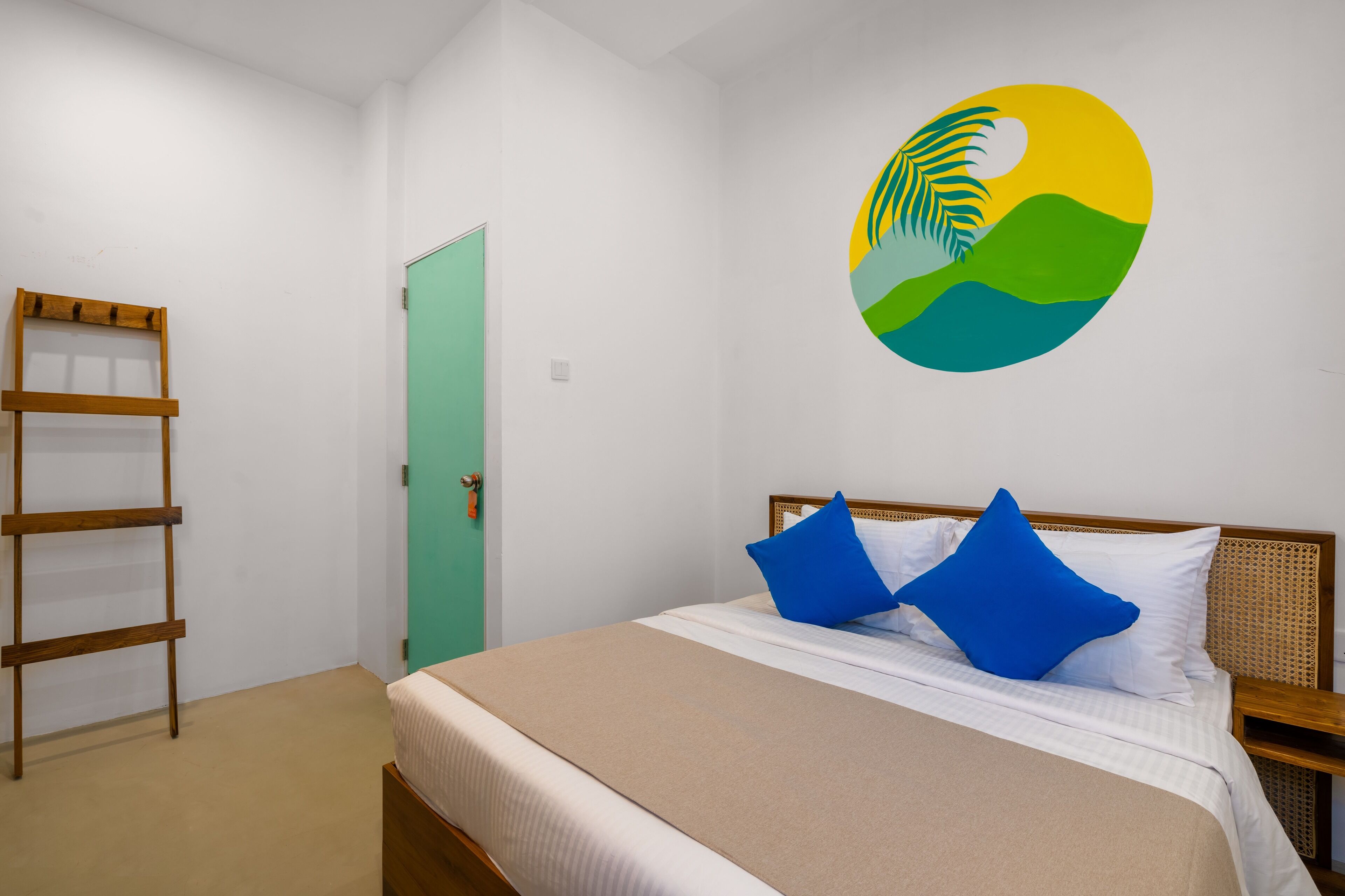 A bedroom with a bed, pillows, a wooden ladder, a green door, and a wall mural.