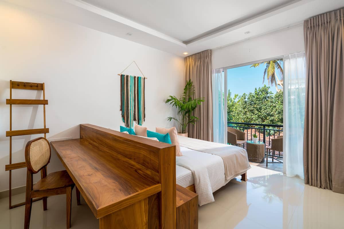 A modern bedroom with a wooden desk, a bed, and a balcony with outdoor furniture.