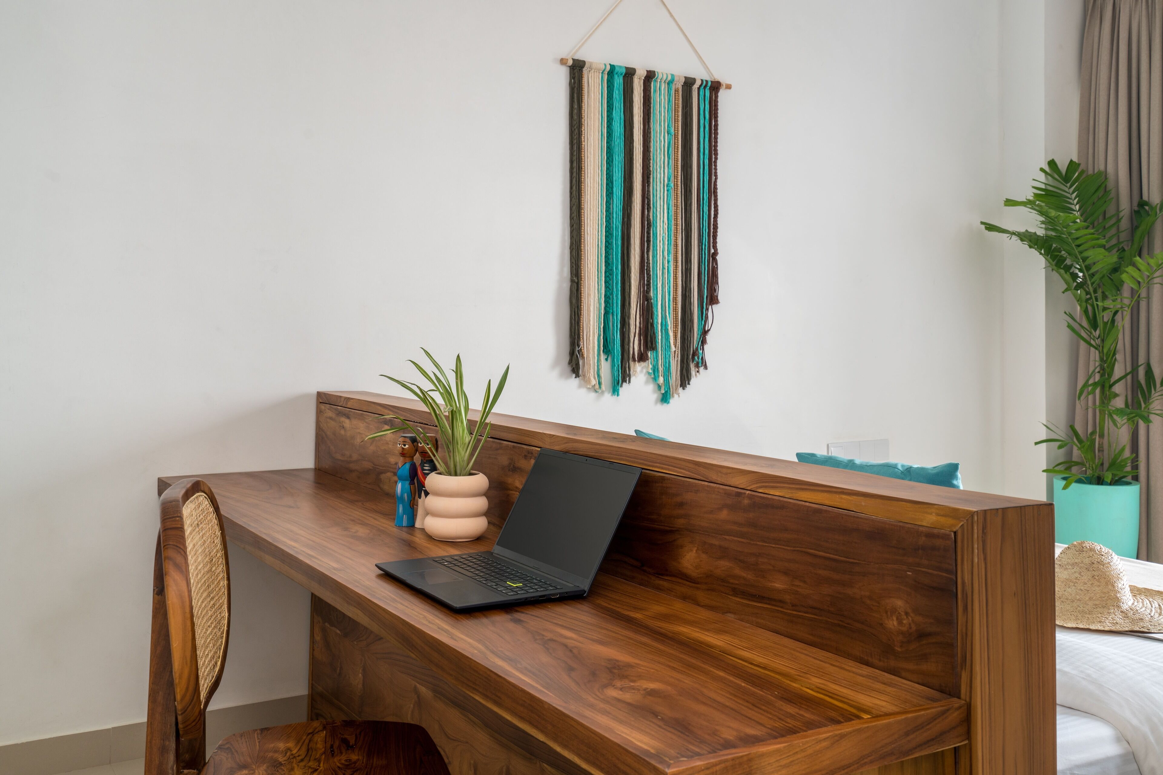 A wooden desk with a laptop, a potted plant, and a wall hanging.