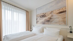 A hotel room with a large bed, a bedside table with a lamp, and a large window with curtains. - Quartier 7, App. 16, Germany (Heringsdorf)