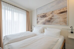 Hotellihuone, jossa on suuri sänky, yöpöytä lampun kanssa ja suuri ikkuna, jossa on verhot.