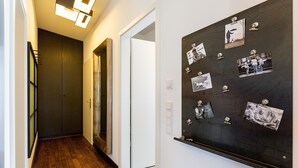 Een gang met houten vloeren, een donkerhouten deur en een prikbord met foto's en aantekeningen.
