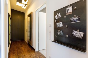 Um corredor com piso de madeira, uma porta de madeira escura e um mural com fotos e anotações.