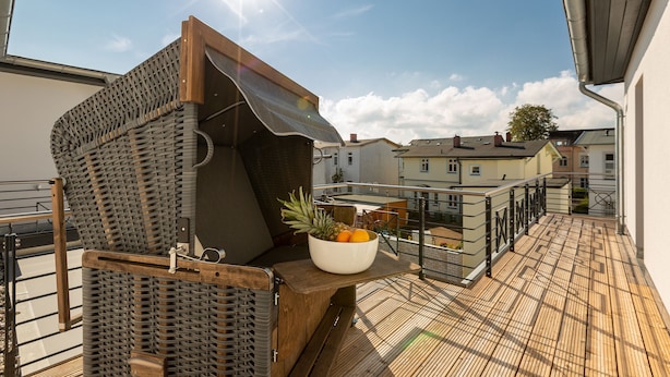 Een balkon met een rieten stoel, een houten tafel en een schaal fruit.