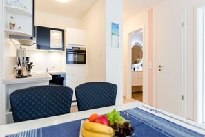 A compact kitchen with modern appliances, a dining area with two chairs, and a table set with fruit.