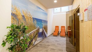 En gang med et mural af et strandmotiv, en trævæg og to orange stole.