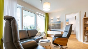 Una sala de estar moderna con un sofá de cuero negro, una silla de madera y una mesita auxiliar blanca.