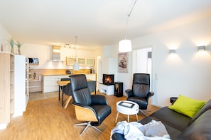 Un salon moderne avec un canapé, deux fauteuils en cuir noir, une petite table blanche et une cheminée.