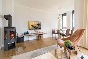 A modern living room with a wood-burning stove, a dining area, and a large window. - Villa Maxim, App. 3, Germany (Heringsdorf)