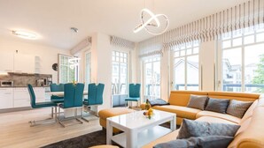 En moderne stue med sofa, stole, et sofabord og et køkken i baggrunden.