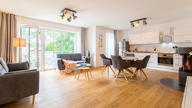 Ein modernes Wohnzimmer mit einer Couch, einem Esstisch und Stühlen, einer Küche mit Geräten und großen Fenstern.