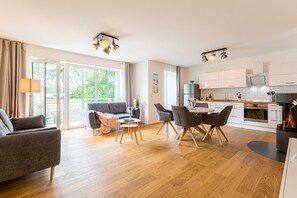 Una sala de estar moderna con sofá, mesa de comedor y sillas, una cocina equipada y ventanas amplias.