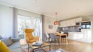 Een moderne woonkamer met een bank, fauteuil, eettafel en een keuken met kasten en apparatuur.