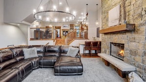 Un salón espacioso con un sofá de cuero grande tipo seccional, una chimenea de piedra y un candelabro moderno.