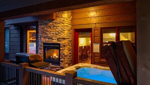 Un espacio exterior acogedor con chimenea de piedra, jacuzzi y terraza de madera.