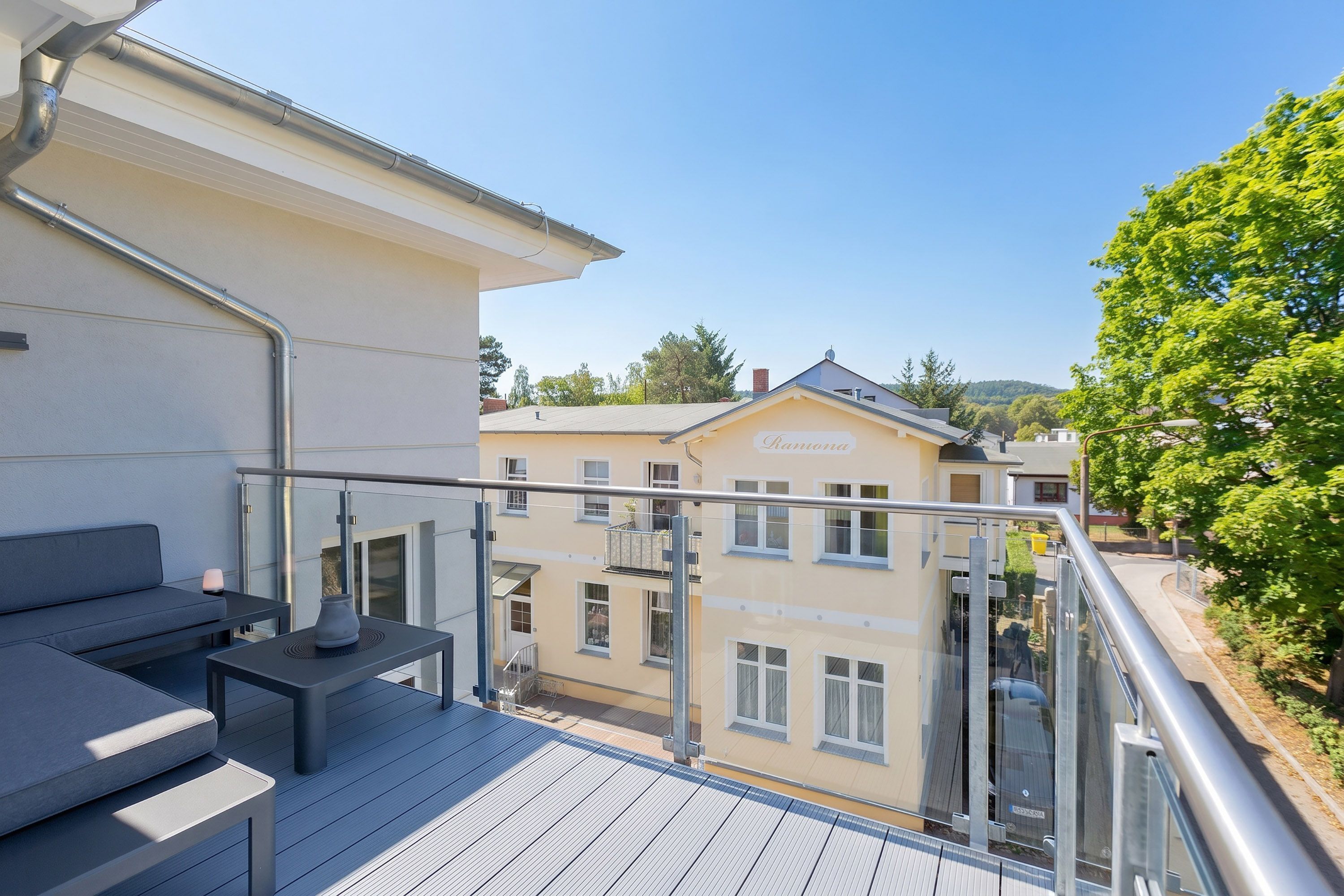 A balcony with a sofa, a table, and a railing overlooking a building with a sign that reads 'Bavaria.'
