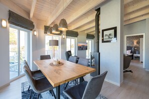 A dining area with a wooden table, chairs, pendant lights, and a view through large windows. - Domicile Düne 8, App. 7 (Heringsdorf)