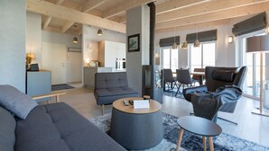 A modern living room with a sofa, coffee table, and a fireplace. There is a kitchen in the background with a dining area. - Domicile Düne 8, App. 7 (Heringsdorf)