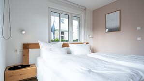 Ein ordentlich bezogenes Bett mit weißen Leinen, einem Holzkopfteil und einem Nachttisch mit einer schwarzen Unterlage.