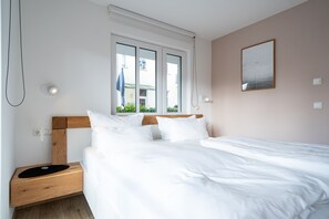 Una cama bien hecha con sábanas blancas, un cabecero de madera y una mesita de noche con un tapete negro.