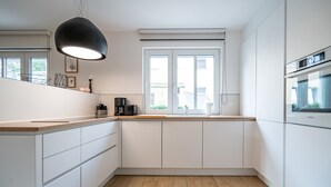 Eine moderne Küche mit weißen Schränken, einer Holz Arbeitsplatte, einem großen Fenster mit Jalousien und einem Bosch-Backofen.
