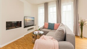 A modern living room with a grey sofa, a flat-screen TV, a coffee table, and a large window with curtains. - Quartier am Kurpark, app. 08 (Heringsdorf)