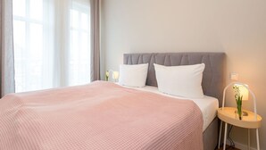 A neatly made bed with a pink bedspread, a grey upholstered headboard, and a bedside lamp with a flower. - Quartier am Kurpark, app. 08 (Heringsdorf)