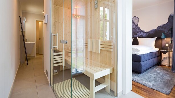 Ein modernes Zimmer mit Glastrennwand, einer hölzernen Bank, einem Bett und Blick ins Freie.